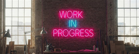 Work in Progress Neon Sign | Bold pink and blue LED neon sign mounted on an industrial brick wall. Perfect for creative workspaces, studios, and motivational decor!