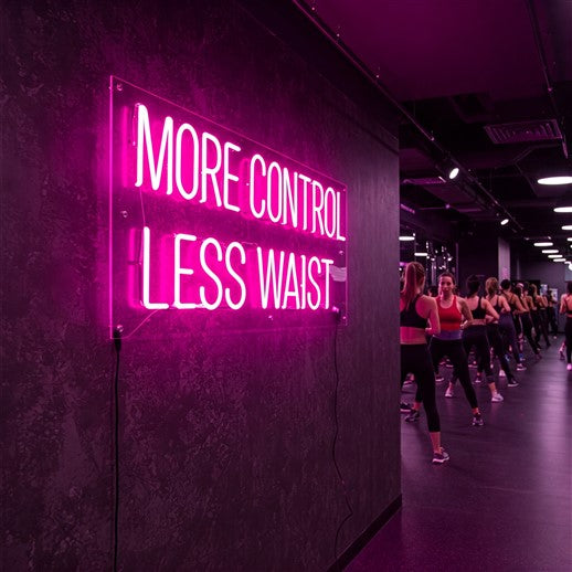 Bright pink LED neon sign reading 'More Control Less Waist' adding a motivational and vibrant touch to a modern fitness studio