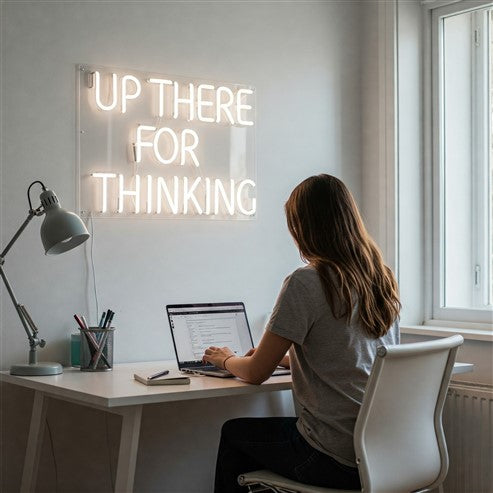 Modern workspace illuminated by a white neon sign reading 'Up there for thinking,' demonstrating how neon signs can enhance focus and style in a home office.