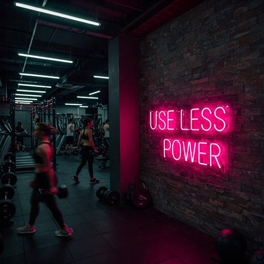 Vibrant pink LED neon sign reading 'Use Less Power' displayed in a modern gym, promoting energy efficiency and sustainability in fitness spaces.